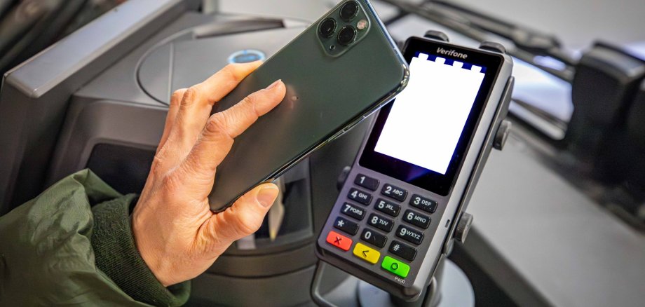 bargeldlos bezahlen in den Bussen der koveb Eine Hand mit Handy, das an ein Cashless-Payment-Terminal im Bus gehalten wird