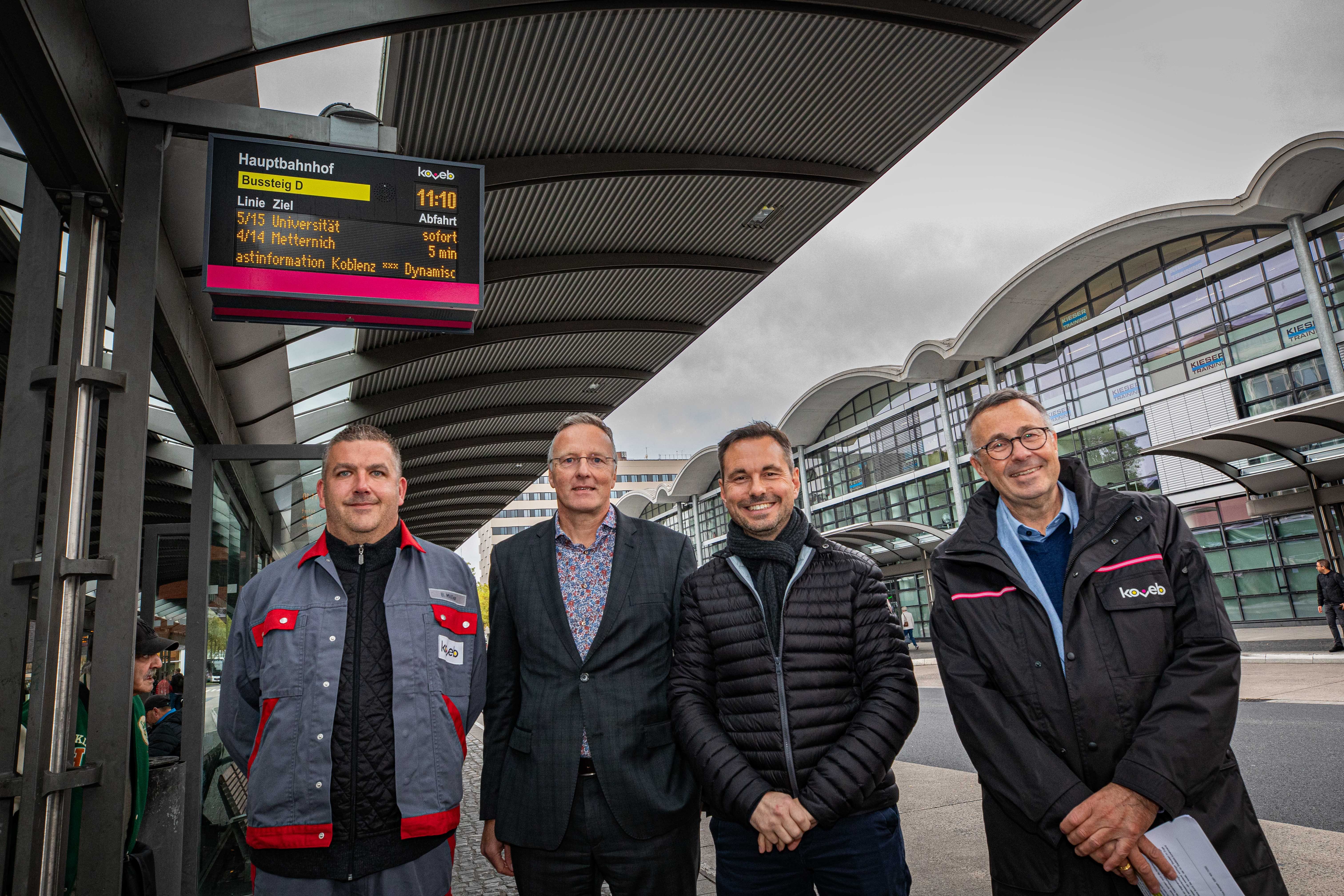 4 Mitarbeiter der koveb feiern fröhlich, dass am Hauptbahnhof neue DFI-Anzeigen aufgehängt wurden.