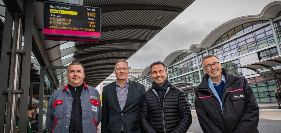 4 Mitarbeiter der koveb feiern fröhlich, dass am Hauptbahnhof neue DFI-Anzeigen aufgehängt wurden.
