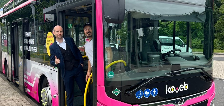 ein fröhlicher Mann steht mit einem lächelnden Busfahrer vor einem Bus der koveb