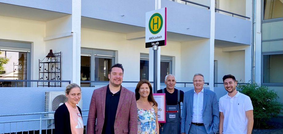 koveb-Mitarbeiter fröhlich vor Bushaltestelle Mitarbeiter von der koveb stehen vor einer passenden Bushaltestelle und freuen sich