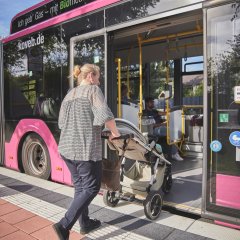 Frau mit Kinderwagen steigt in enen Bus der koveb