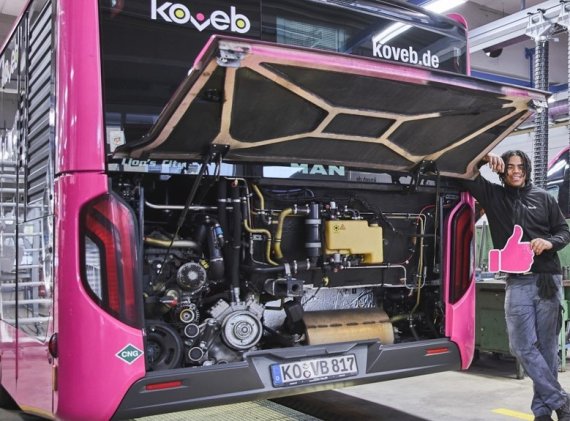 Ein Auszubildender in der koveb-Werkstatt lehnt  an einem koveb-Bus mit geöffneter Motorklappe.
