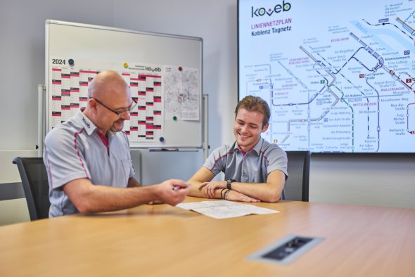 Ein Auszubildender und ein erfahrener Kollege sitzen an einem Tisch während der erfahrene Kollege etwas erklärt.