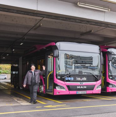 Eine Busfahrerin steigt aus einem Bus und winkt gut gelaunt
