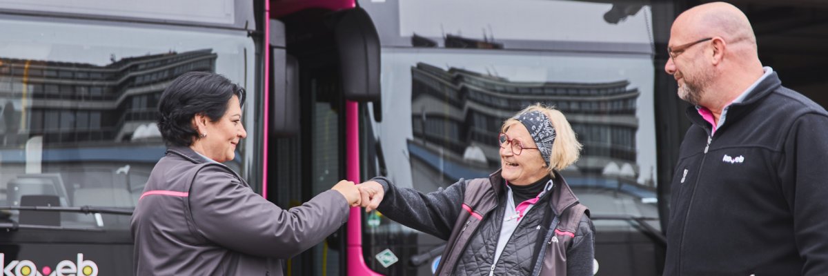 Karriere bei der koveb Zwei Busfahrerinnen begrüßen sich fröhlich. Ein Kollege sieht zu und lächelt.