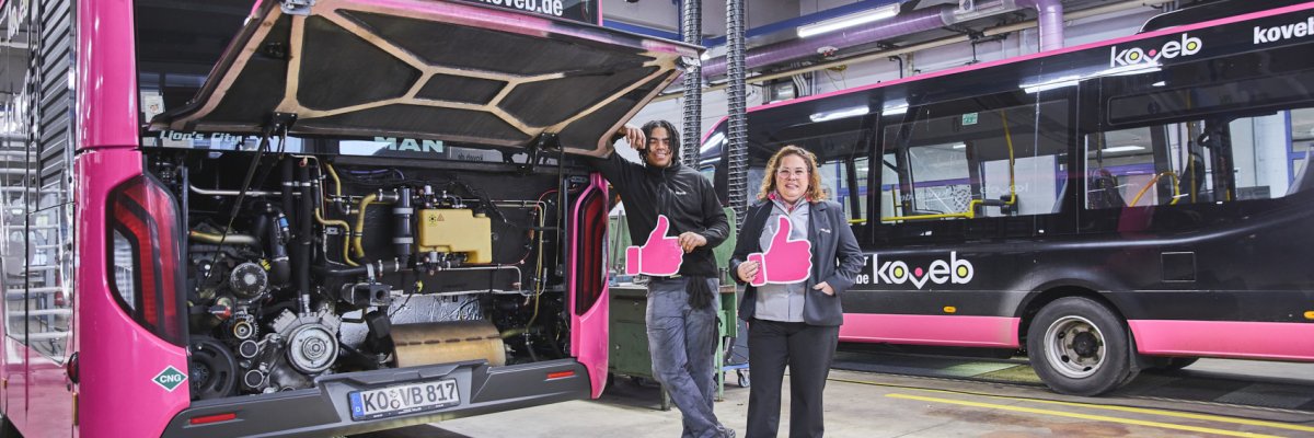 Fachkräfte bei der koveb Eine Mitarbeiterin der Werkstatt und ein Auszubildender stehen neben einem koveb-Bus mit geöffneter Motorhaube und zeigen Daumen hoch.